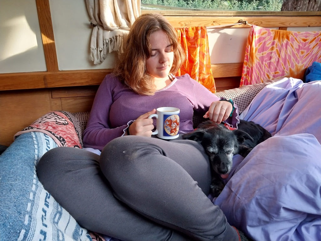 Woman sitting on a couch with a dog, holding a mug, in a cozy living space.