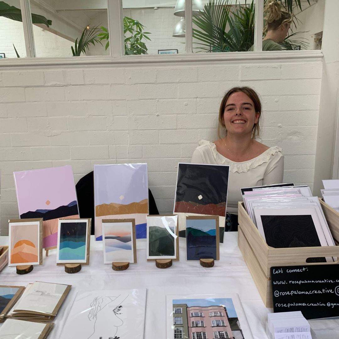 Woman behind a table displaying various art prints in a casual indoor setting.
