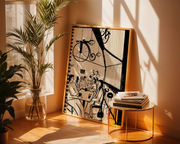 Framed artwork on a wall with a plant and books on a table below.
