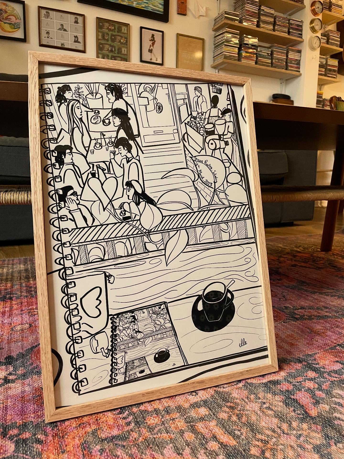 Framed black and white illustration of a cafe scene.