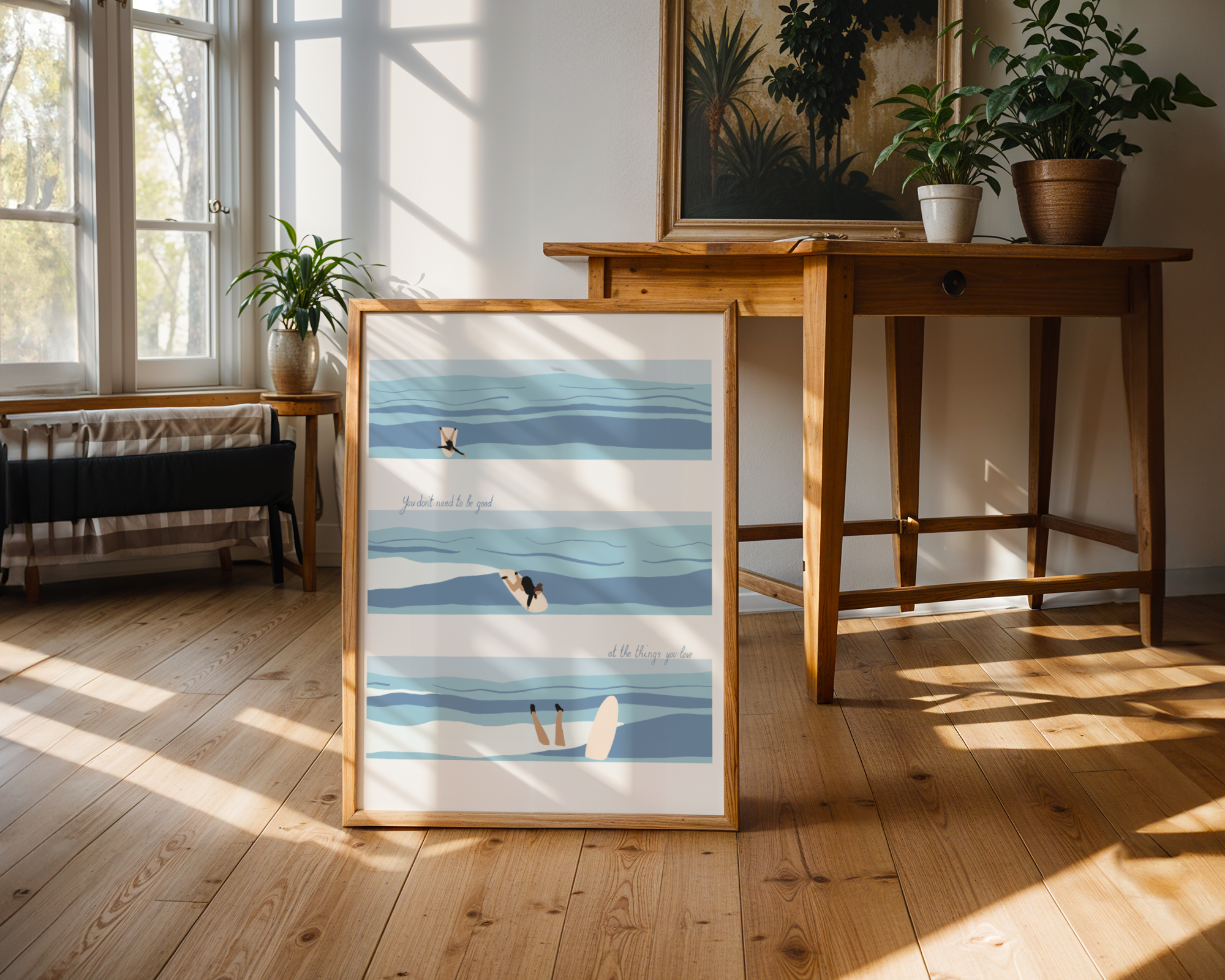 Framed artwork of a beach scene on a wooden floor with a table and plants in the background.
