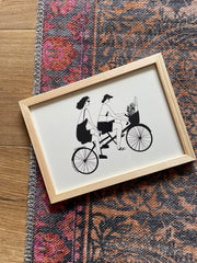 Framed artwork of two people on a tandem bicycle.